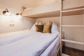 Habitación con literas, una lámpara sobre la litera inferior y un estante de madera en la litera superior.