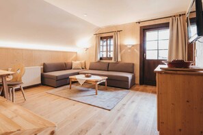 A cozy living room with a sofa, a coffee table, and a dining area with a table and chairs. - Apartment Schwindelfrei - Naturel Hoteldorf SCHÖNLEITN (Latschach am Faaker See)