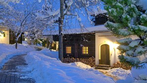 Un sendero cubierto de nieve que lleva a una cabaña de madera con la entrada iluminada y ventanas.