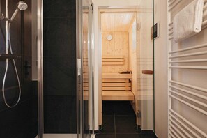 Un baño moderno con cabina de ducha de vidrio, banco de sauna de madera y toallero blanco.