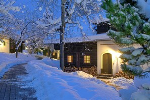 Un sendero cubierto de nieve que lleva a una cabaña de madera con la entrada iluminada y ventanas.