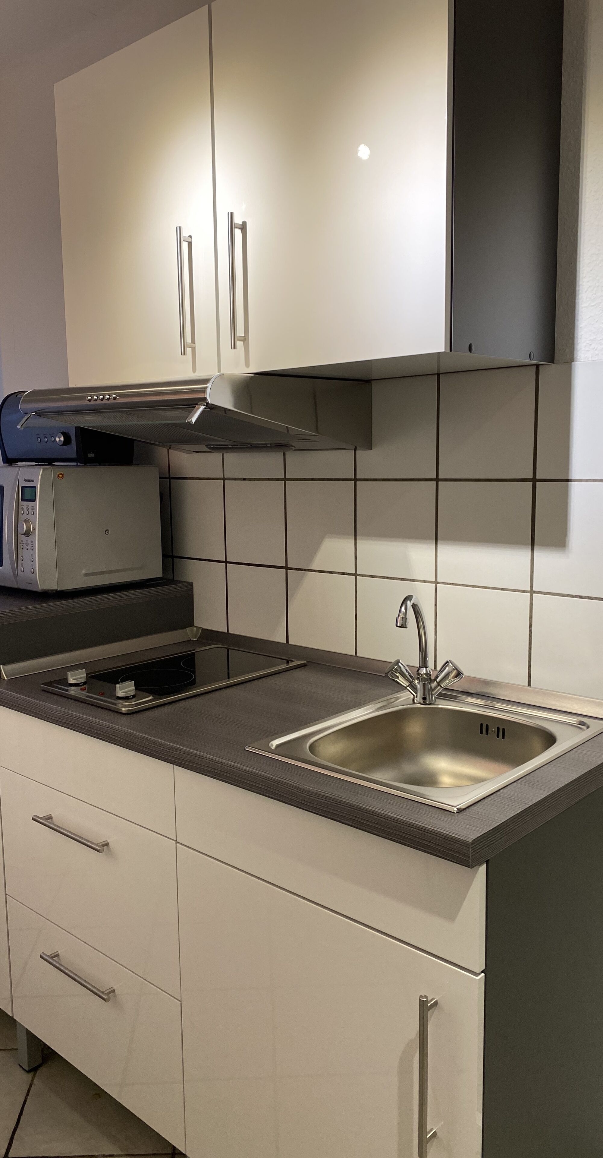 A modern kitchen with white cabinets, a stainless steel sink, and a built-in microwave.