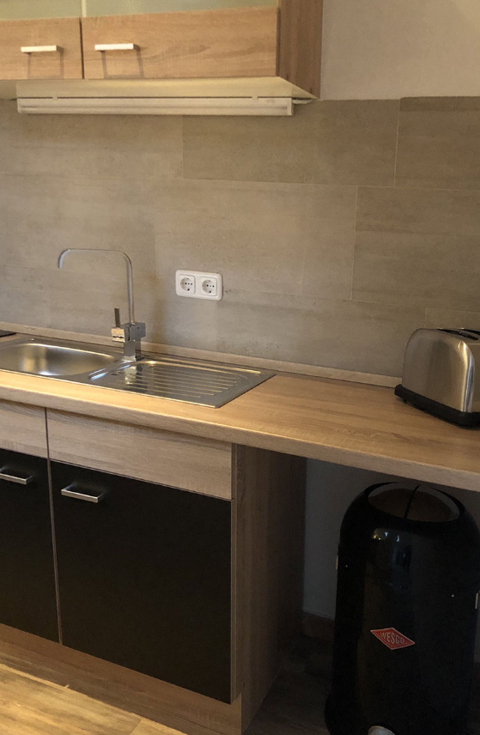 A modern kitchen with a stainless steel sink, wooden cabinets, a toaster, and a black vacuum cleaner.