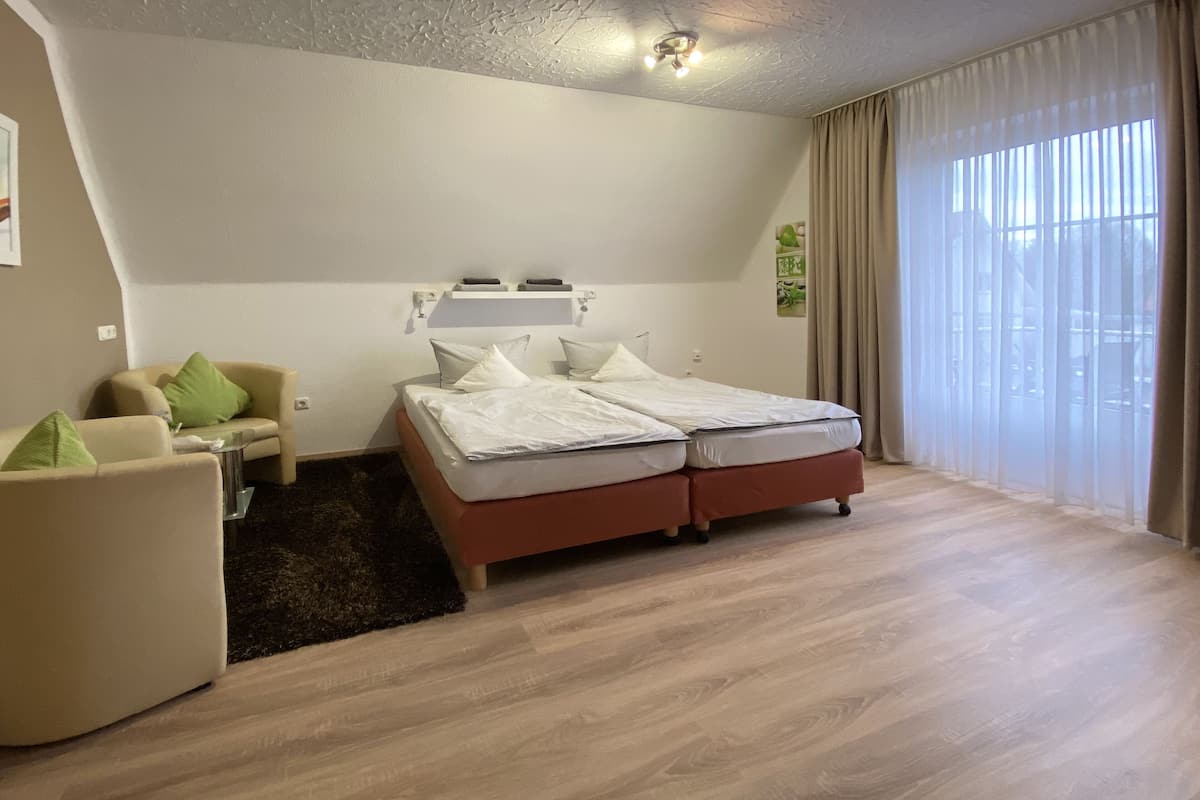 Quarto moderno com cama, sofá, mesa pequena e uma janela grande com cortinas.