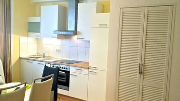A compact kitchen with white cabinets, a stove, and a sink. There are two chairs and a table.
