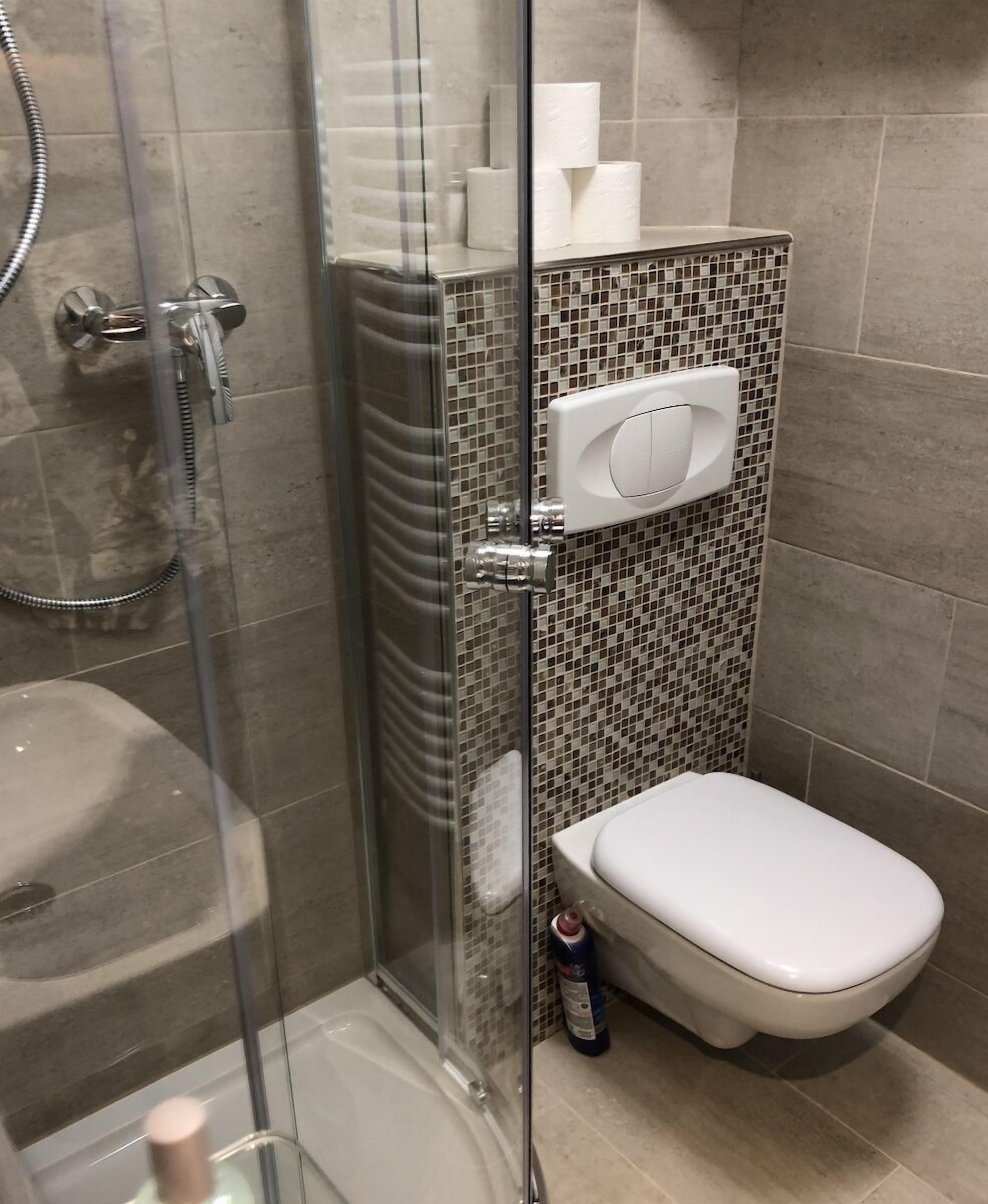 Bagno con doccia vetrata, water e parete rivestita di piastrelle con motivo a mosaico.