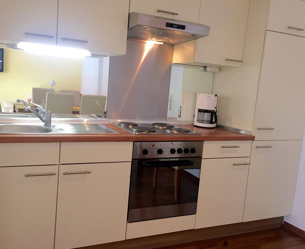 Una cocina compacta con un lavamanos de acero inoxidable, un horno integrado y una cafetera.