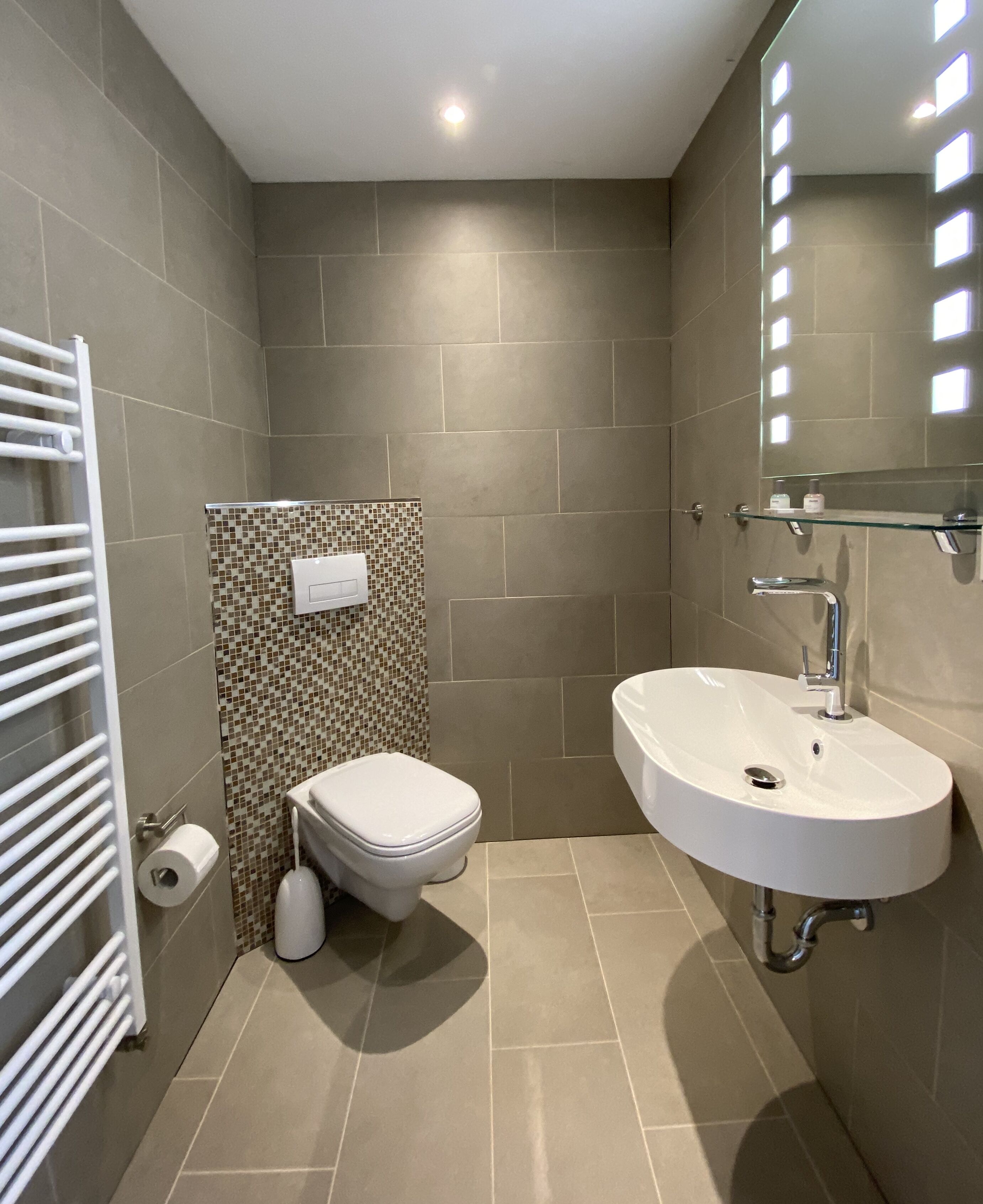 Un bany modern amb un lavabo, un vàter i una barra de tovalloles blancs.