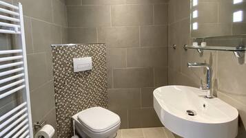 Un bany modern amb un lavabo, un vàter i una barra de tovalloles blancs.