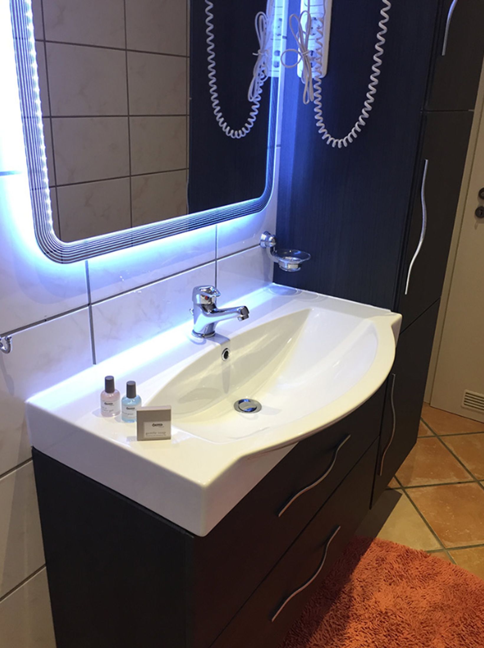 Un baño con lavamanos blanco, un espejo con marco iluminado y un perchero para toallas.