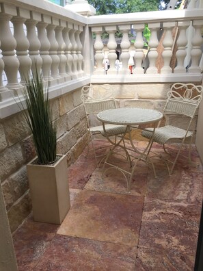 Une terrasse avec un sol en pierre, une table et des chaises en métal blanc, un pot de fleurs et une rambarde décorative.