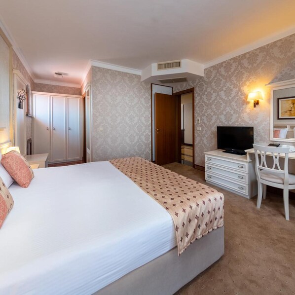 A hotel room with a bed, a desk with a chair, a television, a wardrobe, and a mirror. - Helena Sands (Nessebar)