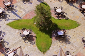 A courtyard with stone flooring, surrounded by outdoor tables and chairs, and a central bush. - Helena Sands (Nessebar)