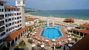 A hotel with a central pool, a clock tower, and a beach view. - Helena Sands (Nessebar)