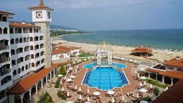 Un hotel con piscina central, una torre del reloj y vista al mar.