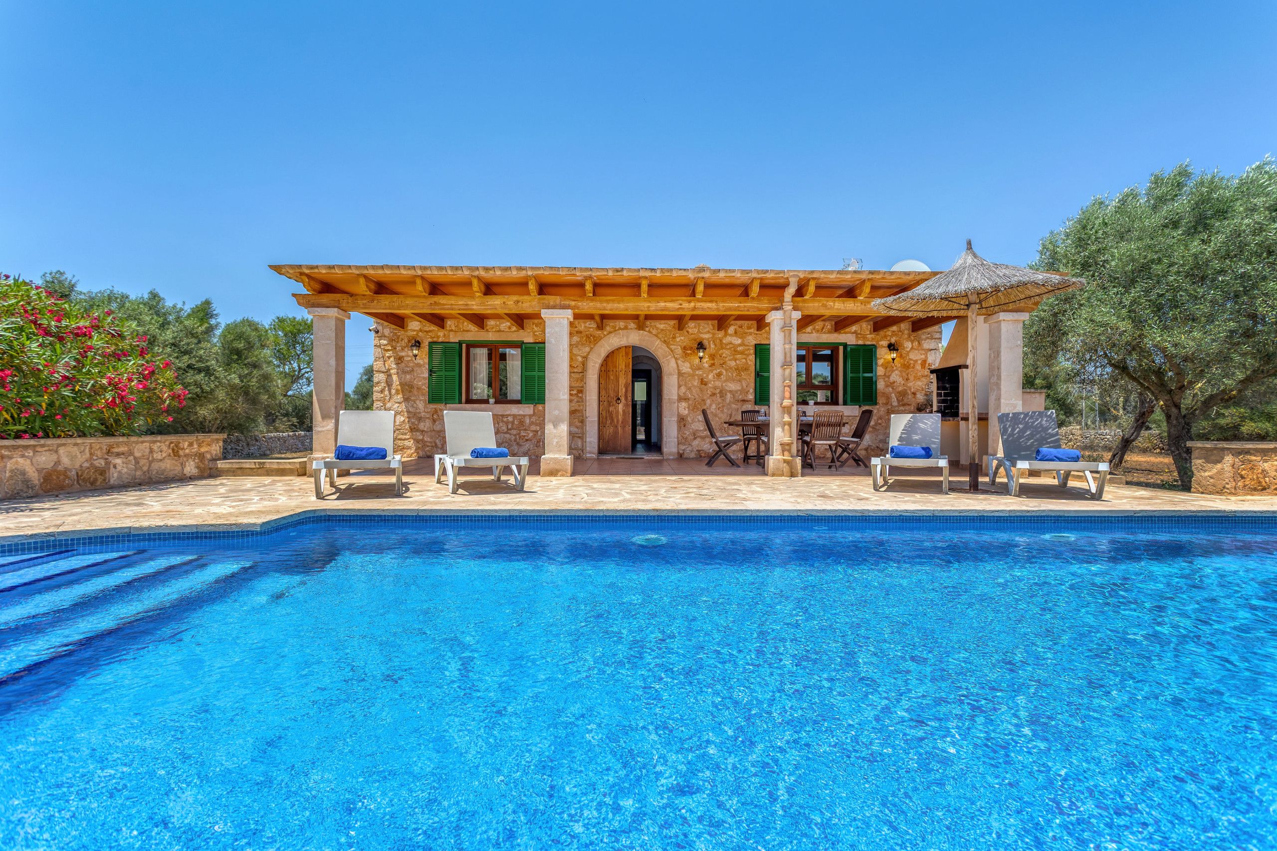 A poolside area with a stone building, outdoor seating, and a clear blue pool.