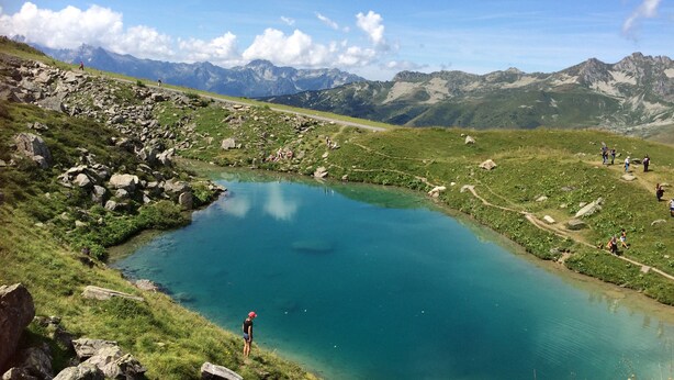 Un paisaje montañoso con un lago cristalino, terreno rocoso y montañas distantes.