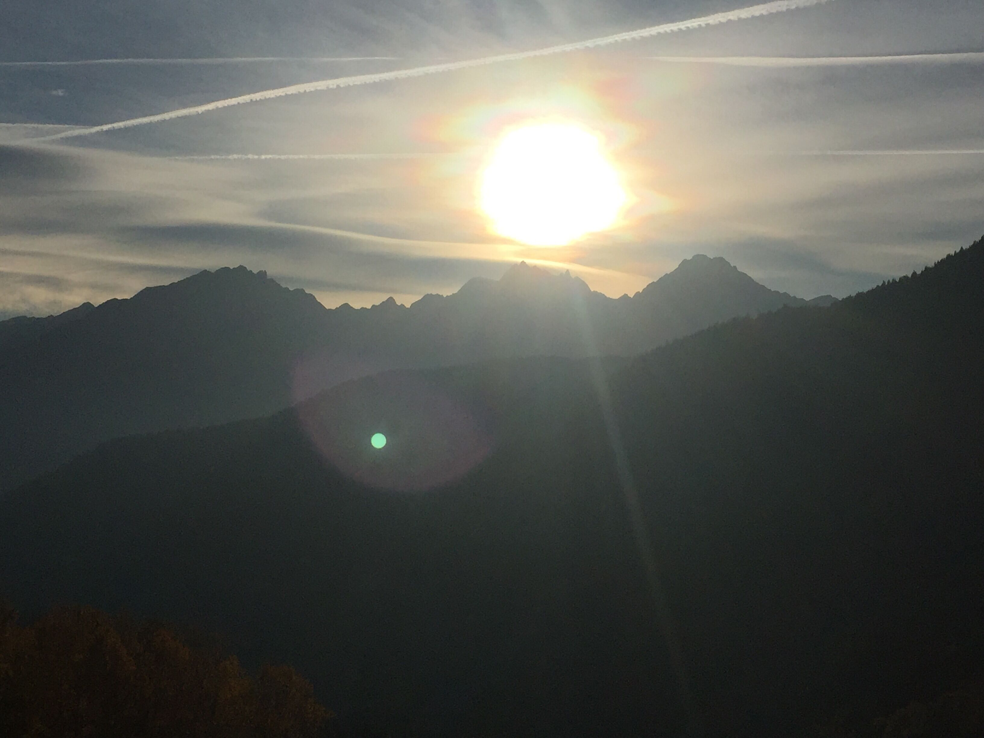 A mountain landscape with the sun setting behind the peaks.