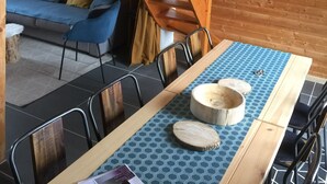Un interior de madera con una mesa de comedor, sillas, mantel azul estampado y una escalera de madera.