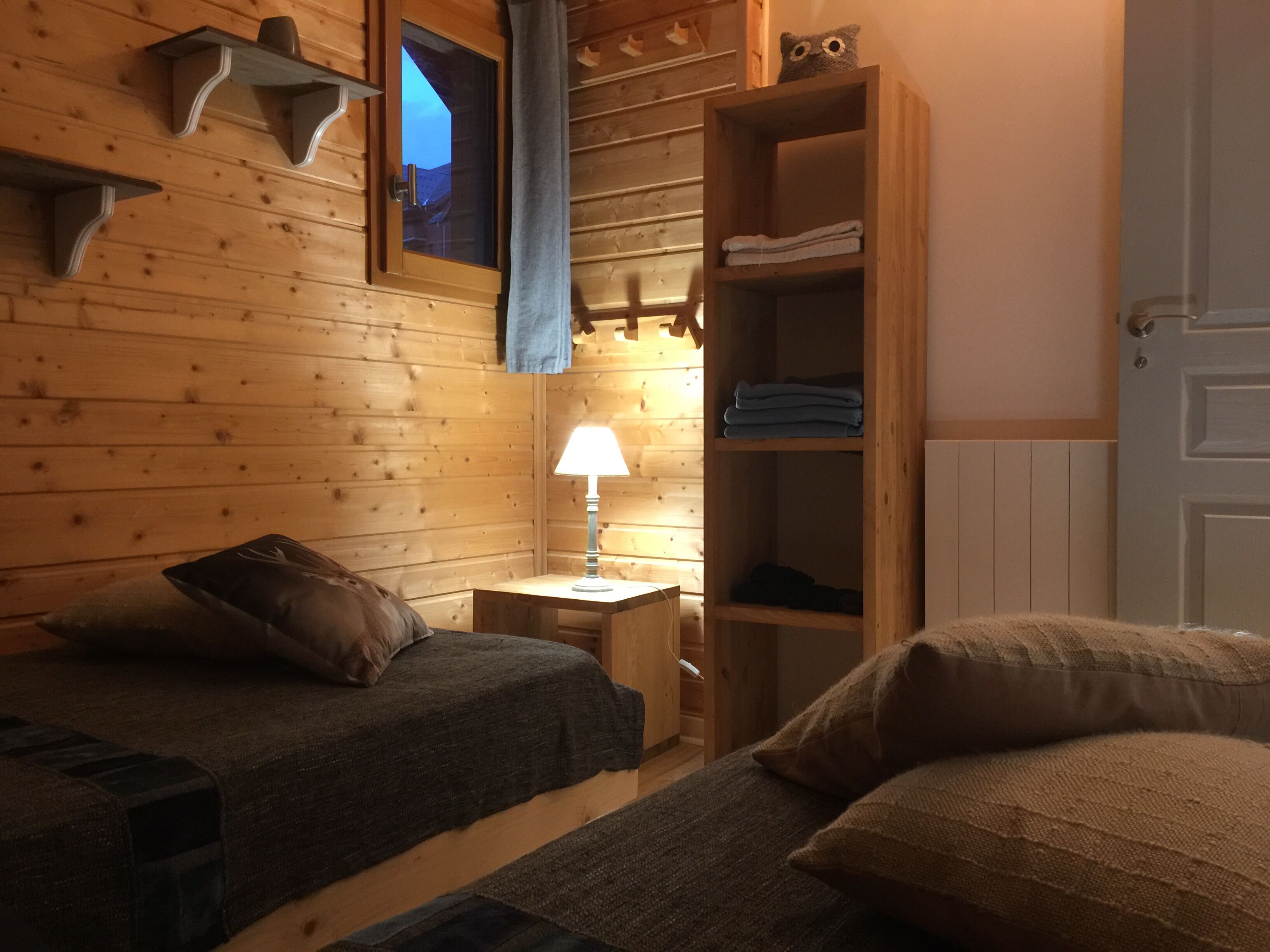 Una habitación acogedora con dos camas, una mesita de noche, una lámpara, un armario de madera y una ventana con cortinas.
