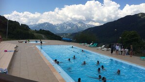 Una piscina con gente en el agua, rodeada de montañas y un cielo despejado.