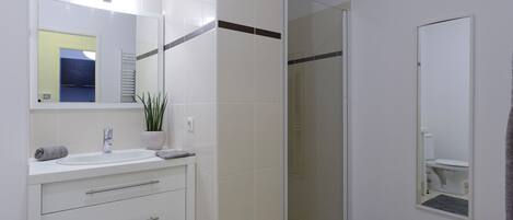 Un baño moderno con tocador blanco, cabina de ducha de vidrio y espejo.