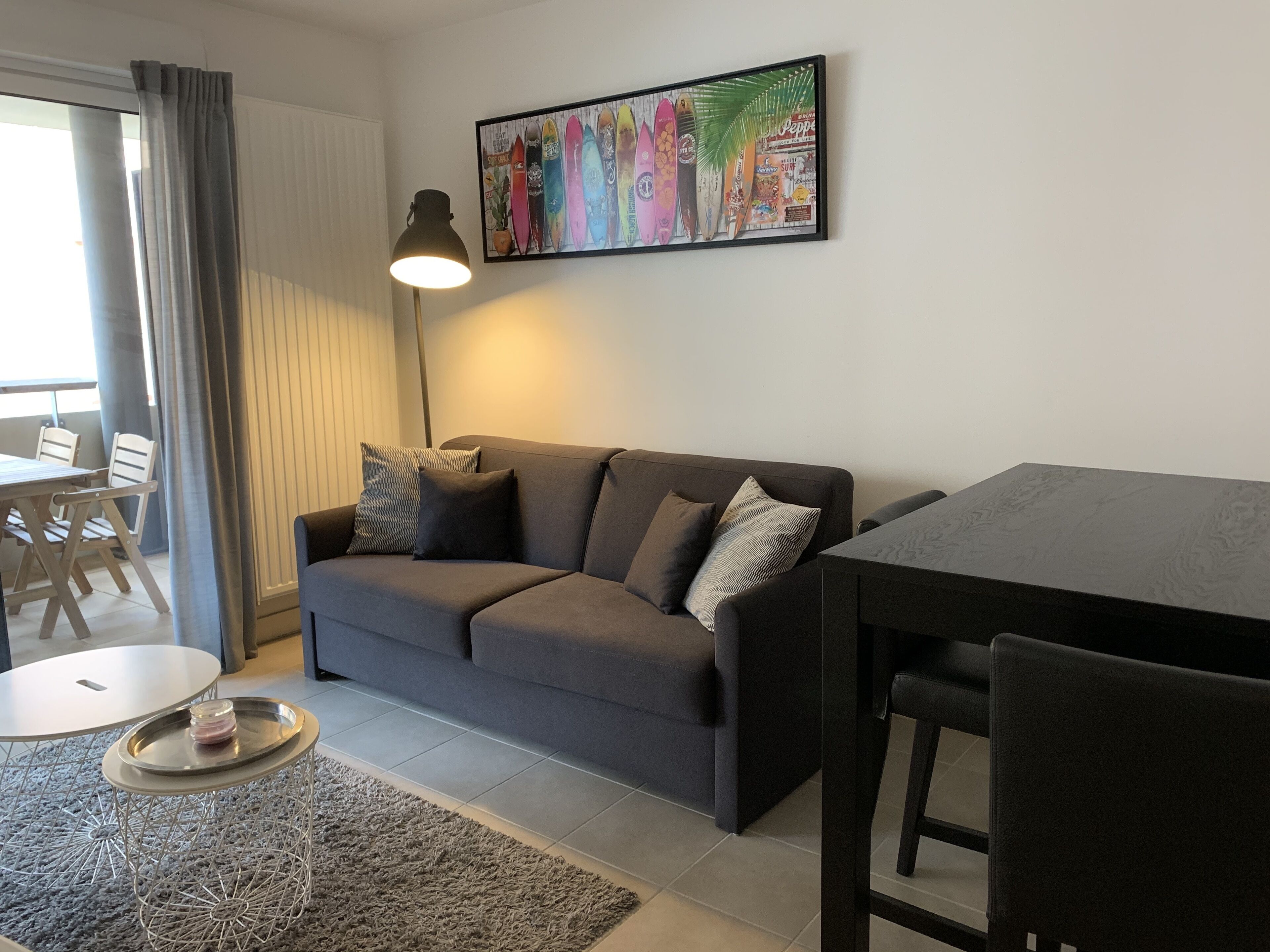 Una sala de estar moderna con un sofá gris, una mesa de comedor y una lámpara de pie.