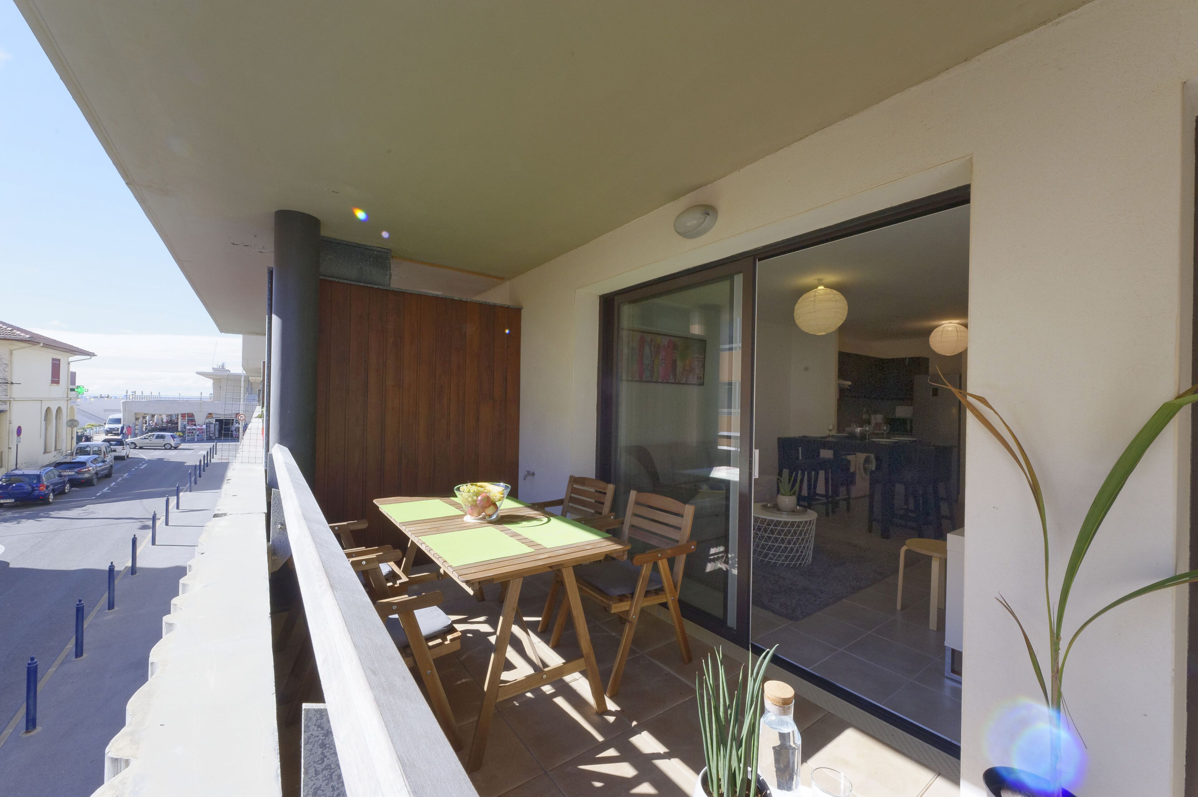 Un balcón con una mesa y sillas, vista a la calle y un vistazo al interior.