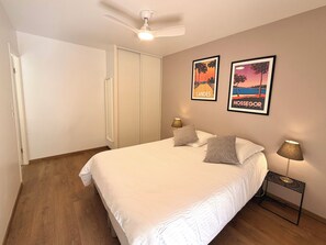 Un dormitorio con una cama, un ventilador de techo, dos lámparas fijadas a la pared y dos cuadros enmarcados.