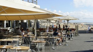An outdoor café with tables and chairs under umbrellas, overlooking a beach.