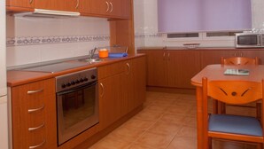 Une cuisine avec des meubles de rangement en bois, une cuisinière, un four à micro-ondes et une table à manger avec des chaises.