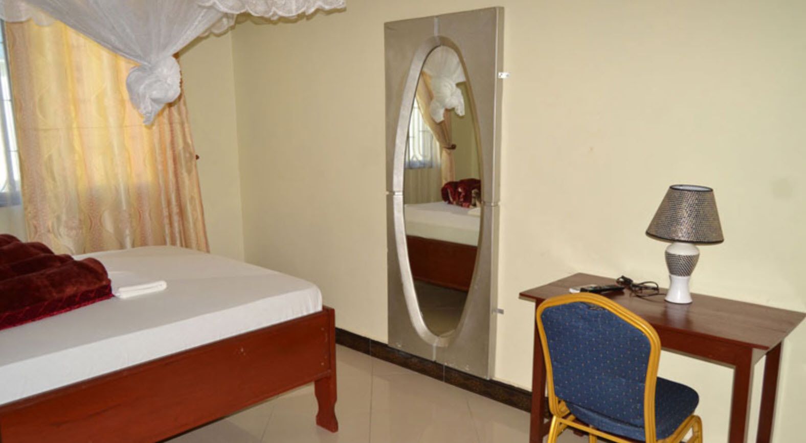 Un dormitorio con cama, espejo, escritorio con lámpara y silla.