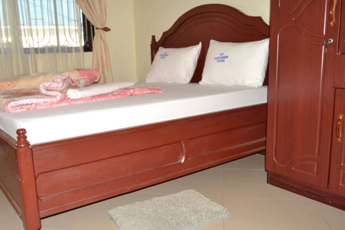 Una cama de madera con ropa de cama blanca, una alfombra pequeña y un armario de madera.