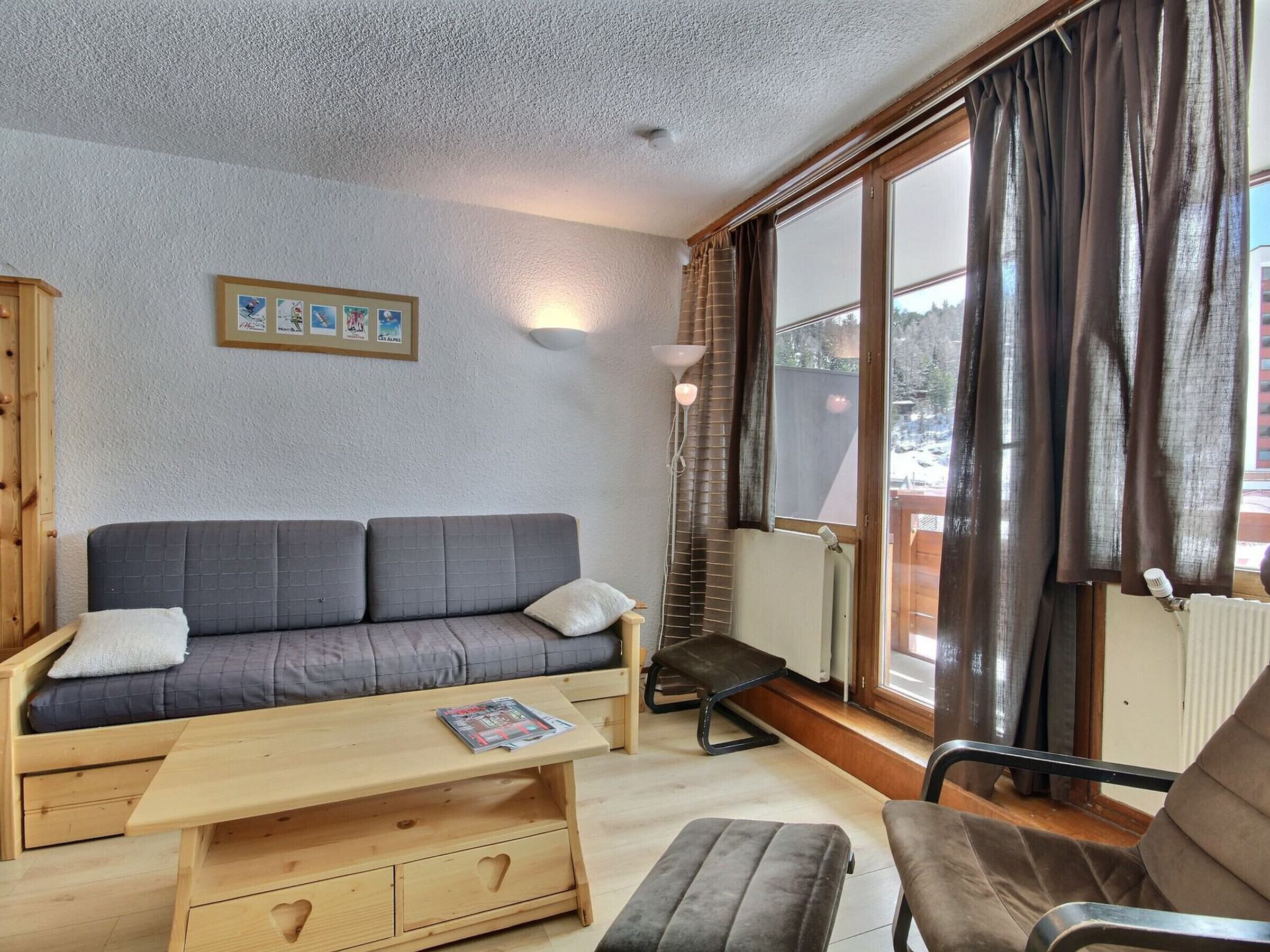 Une pièce chaleureuse avec un canapé, une table basse en bois, un banc et une chaise. Il y a une fenêtre avec des rideaux et un radiateur.