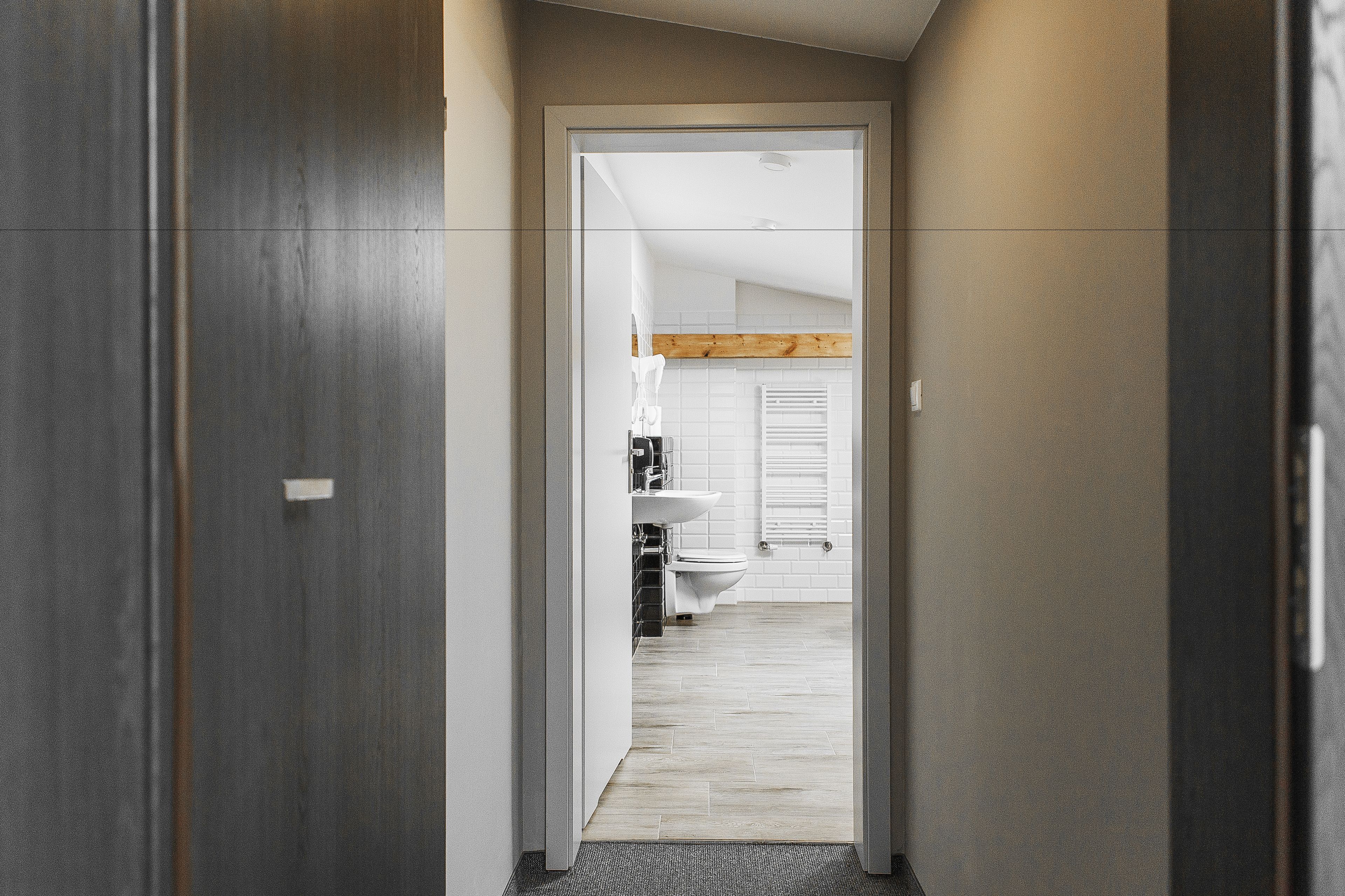 A hallway leading to a bathroom with a wooden ceiling and white tiles.