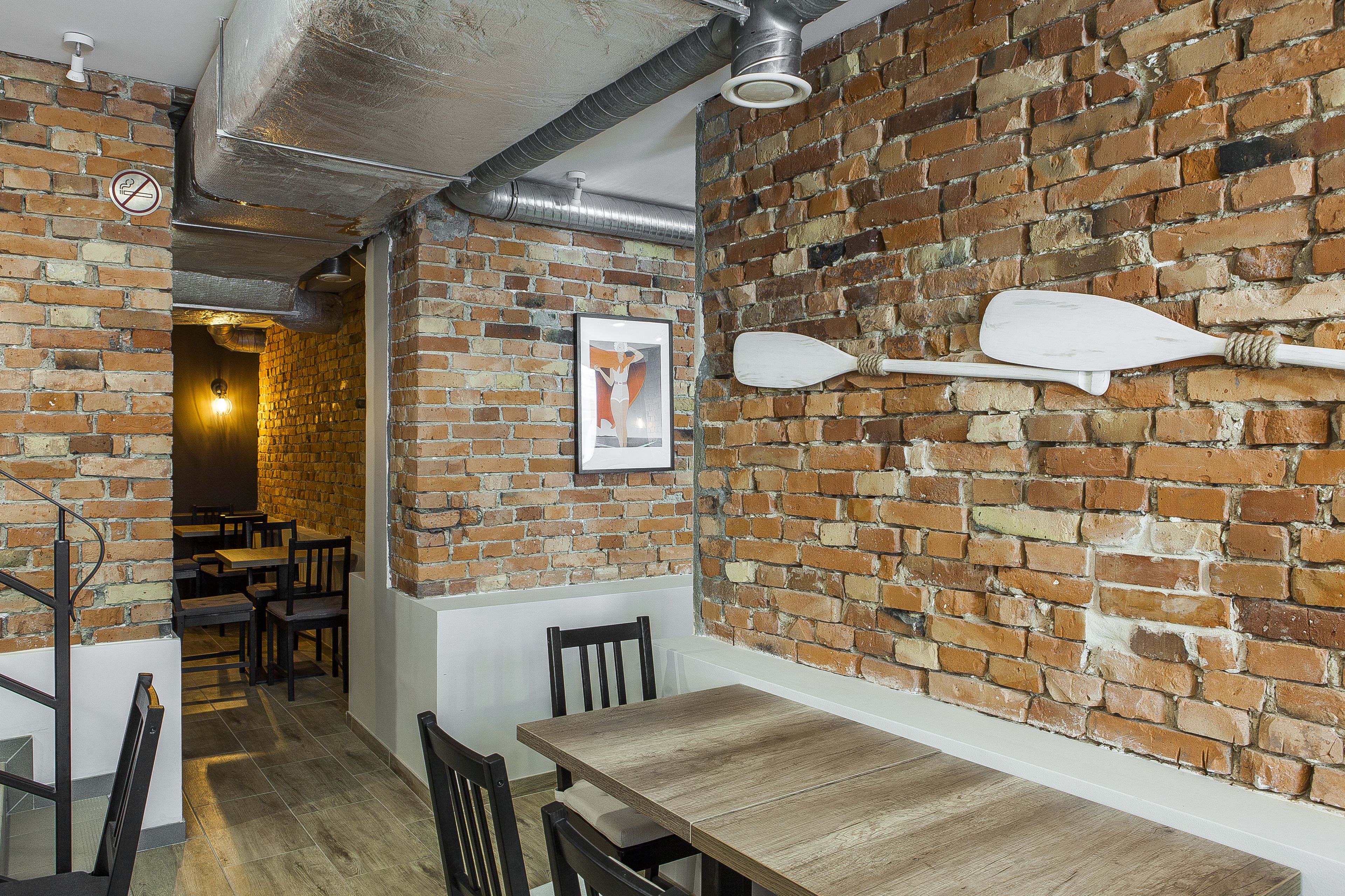 A brick-walled interior with a wooden table and chairs, a white paddle, and a framed picture on the wall.