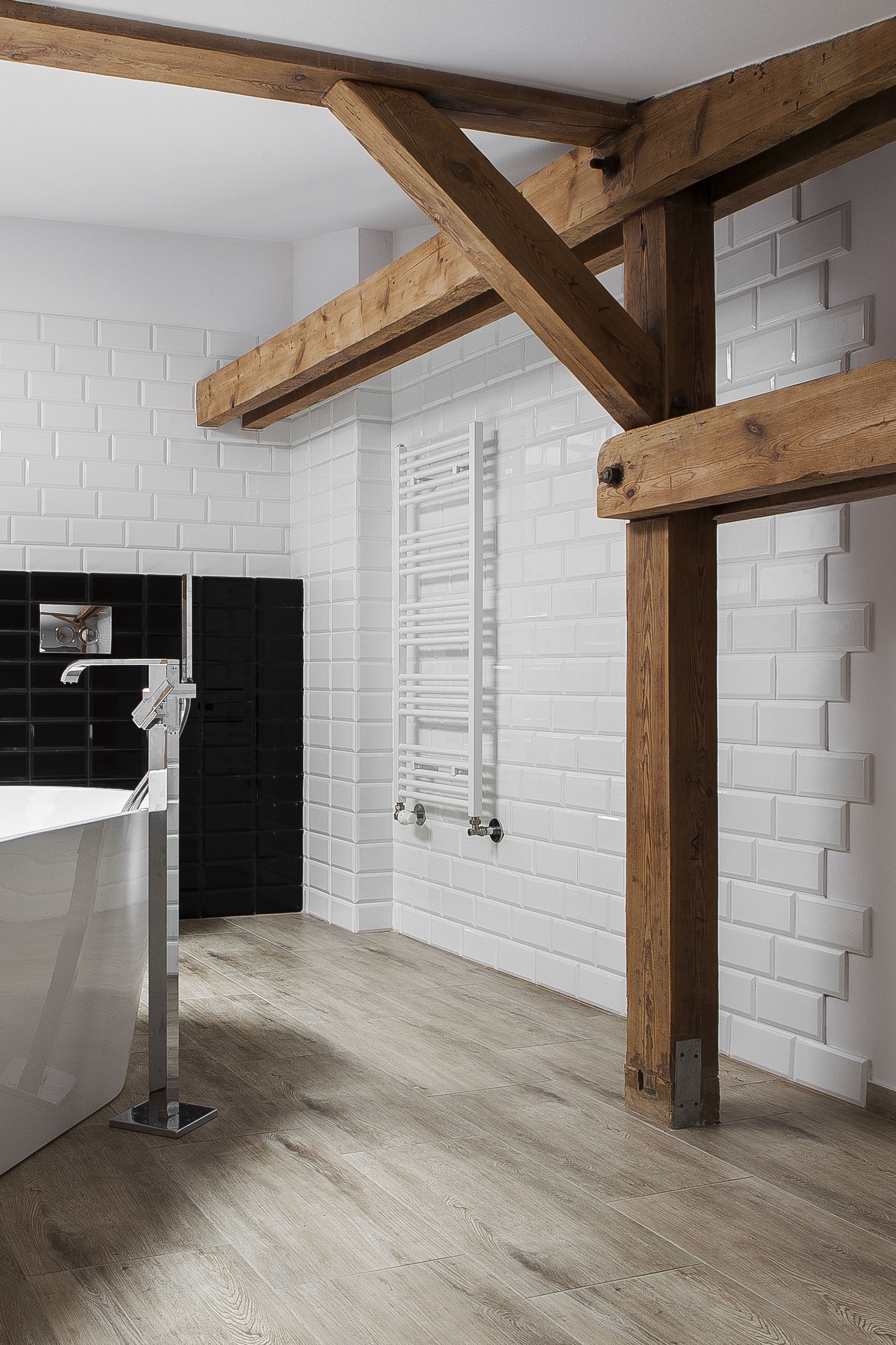 Un ba ño moderno con azulejos blancos tipo metro, una viga de techo de madera, un lavabo blanco y un respuesto de azulejos negros.