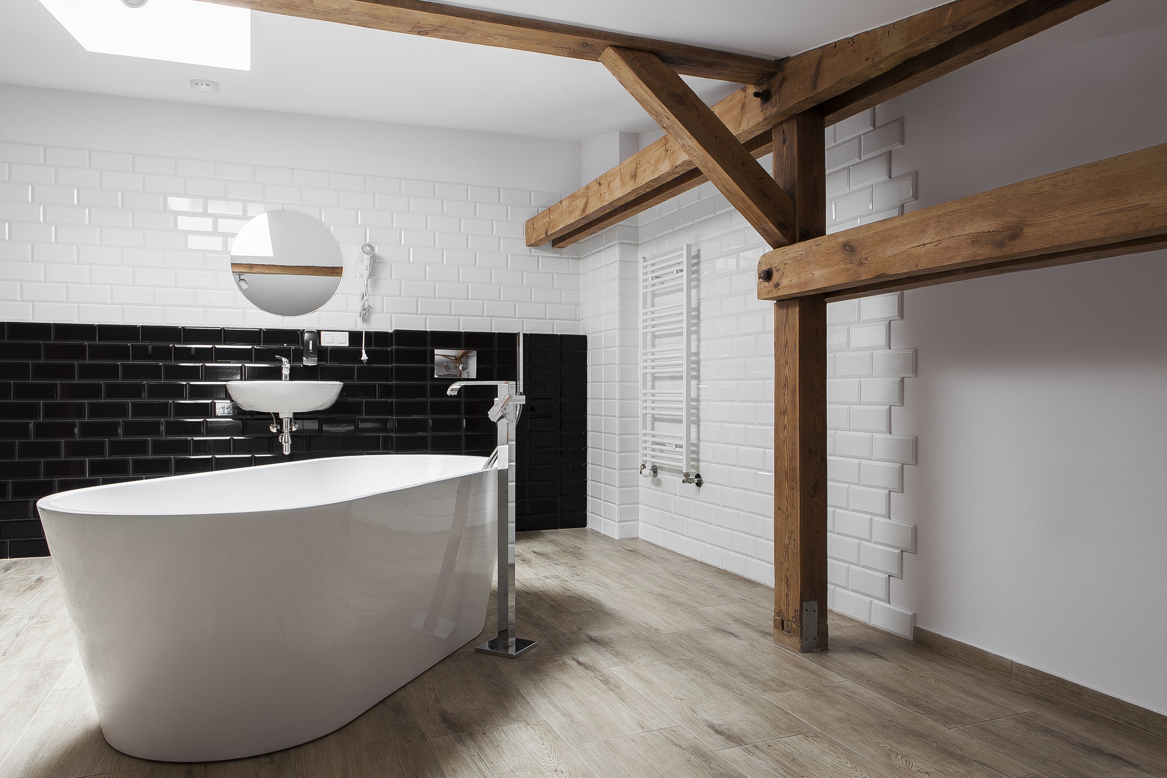 Une salle de bain moderne avec une baignoire sur pieds, un miroir rond et un mur recouvert de carreaux noirs et blancs.