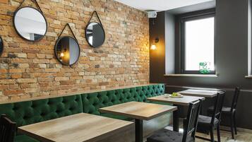 Un restaurante con pared de ladrillo, banco tapizado en verde, mesas de madera y sillas negras.