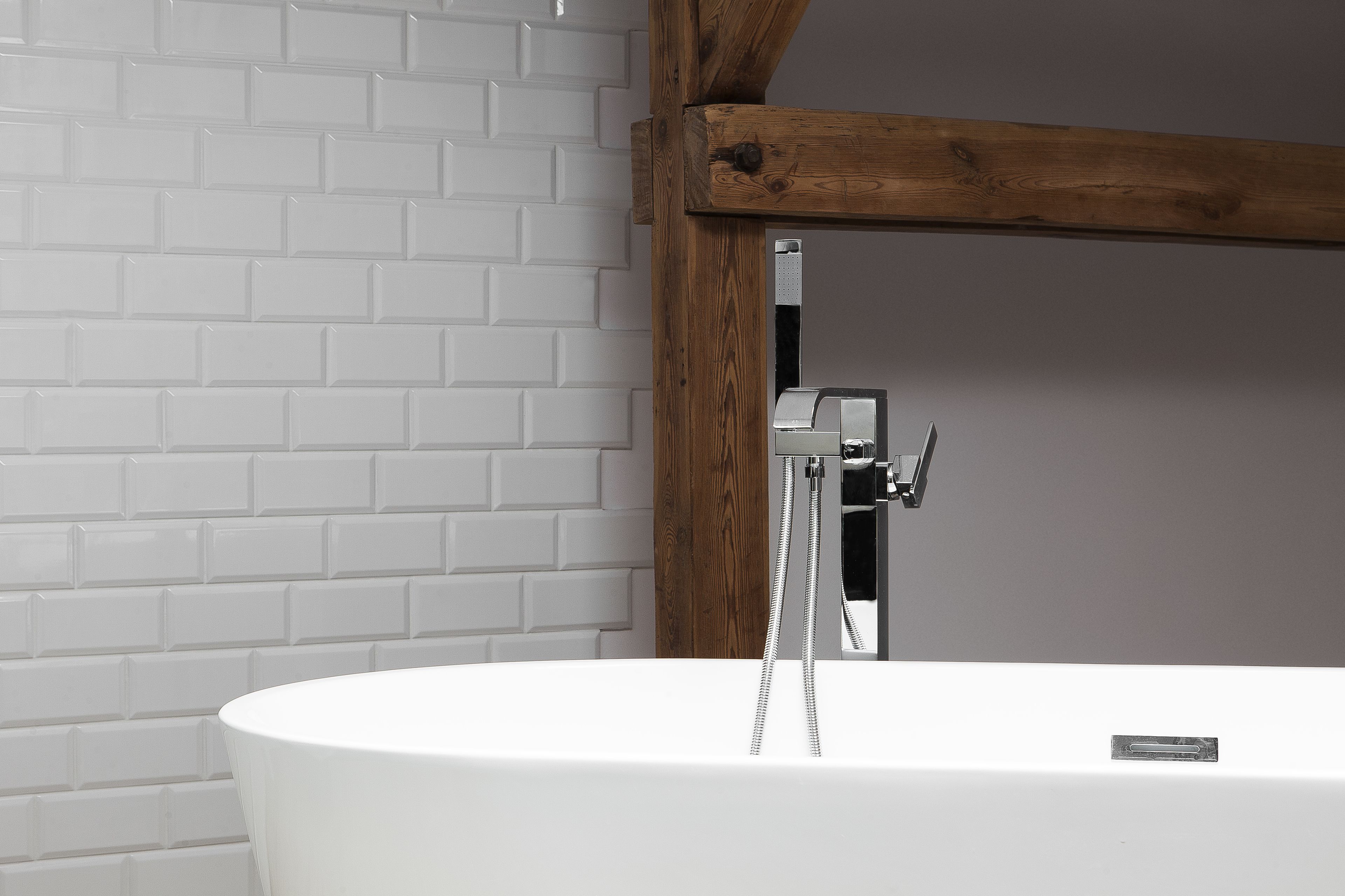 A modern bathroom with a white bathtub, wooden beams, and a white tiled wall.