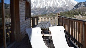 A wooden deck with two white lounge chairs facing a mountain view.