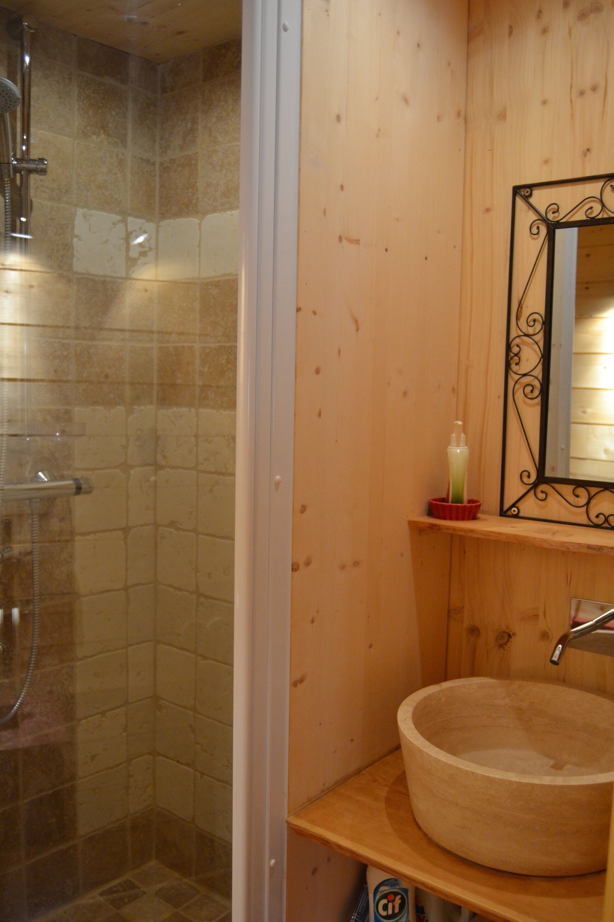 A bathroom with a wooden vanity, a round sink, and a glass shower enclosure.