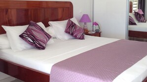 Une chambre d’hôtel avec un lit en bois, du linge de lit blanc et des oreillers violets.