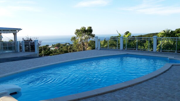 Une piscine avec vue sur l’océan, entourée d’une clôture blanche et de verdure.