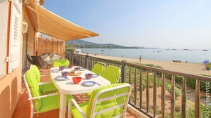 A balcony with a table set for dining, overlooking a beach with boats and people. - Large 3 Bedrooms flat with superb sea view (PORT GRIMAUD)