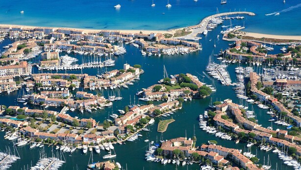 An aerial view of a coastal town with numerous boats docked in a marina, surrounded by residential buildings with terracotta roofs. - Large 3 Bedrooms flat with superb sea view (PORT GRIMAUD)