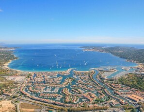 An aerial view of a coastal town with a marina filled with boats, surrounded by residential buildings and a clear blue sky. - Large 3 Bedrooms flat with superb sea view (PORT GRIMAUD)
