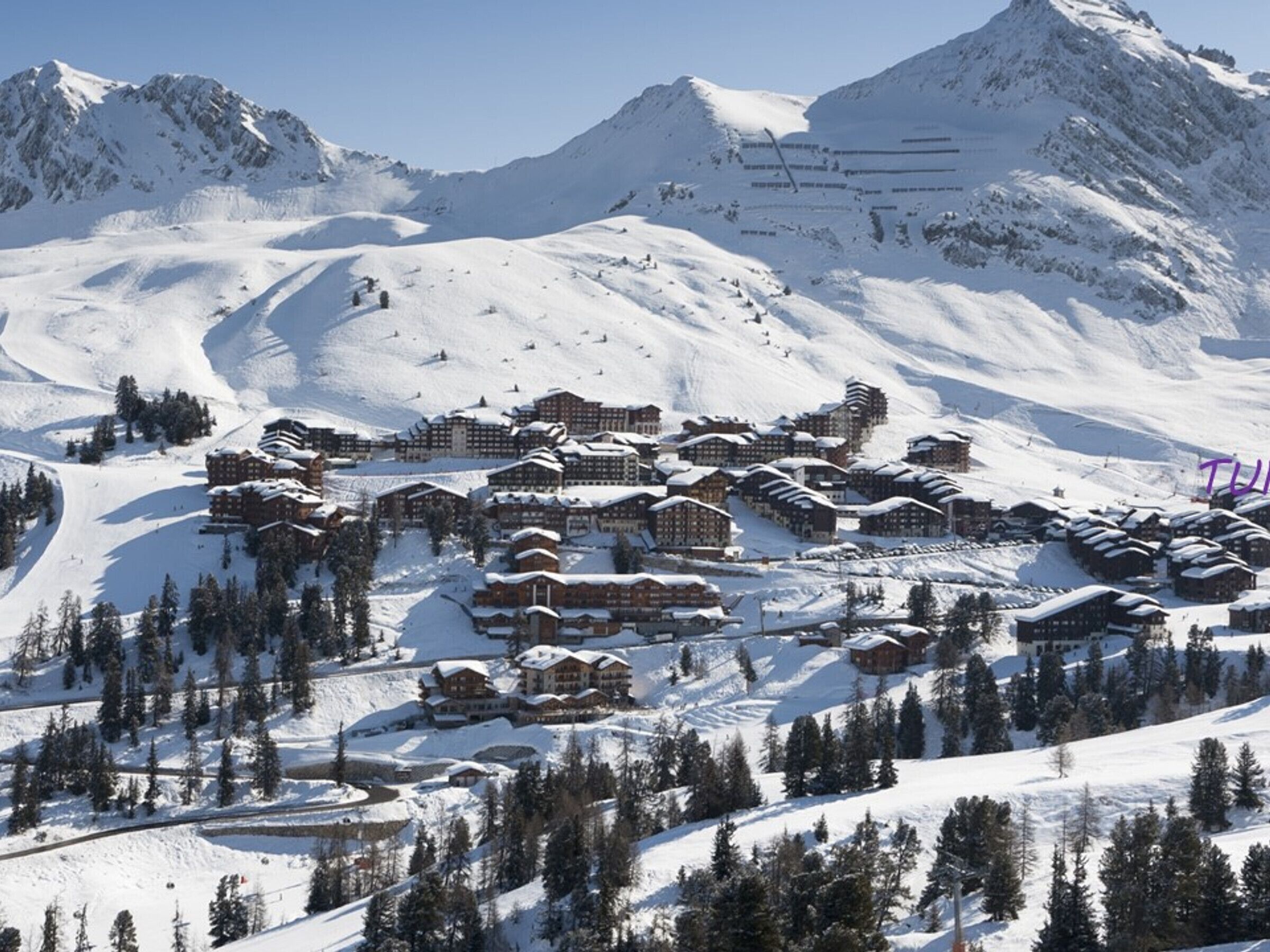 A snow-covered mountain resort with multiple chalet-style buildings, ski slopes, and pine trees.