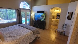 Ein Schlafzimmer mit einem großen Bett, einem Fernseher und Blick auf einen Pool und Berge durch ein Fenster.