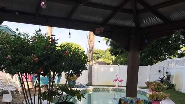 Un patio al aire libre con zona de estar techada, piscina y plantas en macetas.